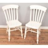 A pair of white painted kitchen chairs.