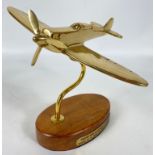A Desk top brass model of a SPITFIRE on wooden plinth with inscription ''Never was so much owed by