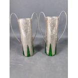 An UNUSUAL pair of twin-handled vases made from beaten white metal with fitted green glass liners