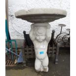 A very old two piece bird bath consisting of a small boy holding up the bath which has been
