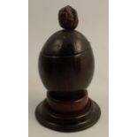 A 19th century coconut shell tea caddy, standing on a stepped wooden base, and having a walnut as