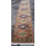 A wool runner, decorated with lozenges to a peach ground, 133ins x 32ins