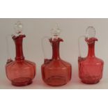 Three cranberry glass decanters, with clear glass stoppers, height 10.75ins and down