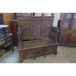An oak box seat settle, having thee panels to the back, carved with shields, fruiting vine and