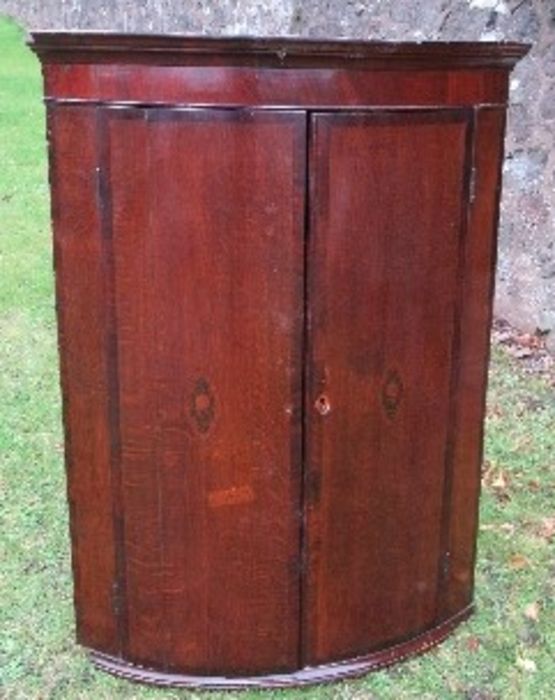 A Georgian oak bow front corner cupboard, the doors having inlaid decoration, opening to reveal