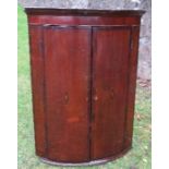 A Georgian oak bow front corner cupboard, the doors having inlaid decoration, opening to reveal