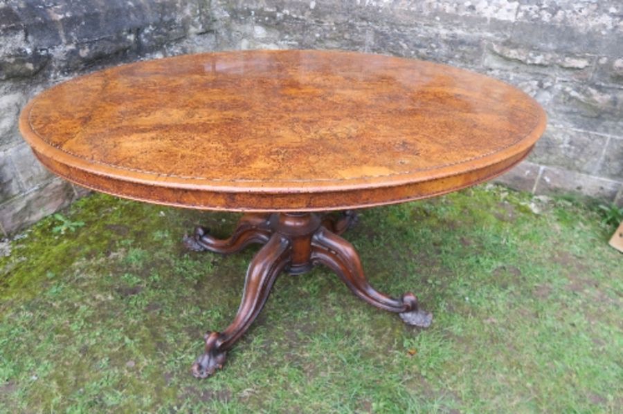 A 19th century burr walnut oval loo table, raised on a turned column, terminating in four outswept