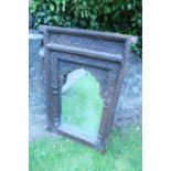 A primitive carved oak mirror, with arcaded top, below a motif carved frieze, and the mirror flanked