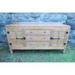 An oak sideboard, having three drawers flanked by a four panel door, to each side, below an adzed