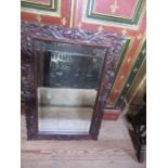 An Arts and Crafts carved oak mirror, having a bevelled glass plate, surrounded by a relief carved