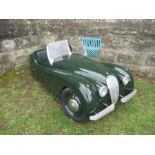 A toy swing pedal car, in the style of a Jaguar XK120, in British racing green, 66ins x 24ins