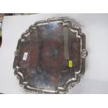 A silver salver, of shaped square form, with ogee and shell edge, raise don four scroll feet,