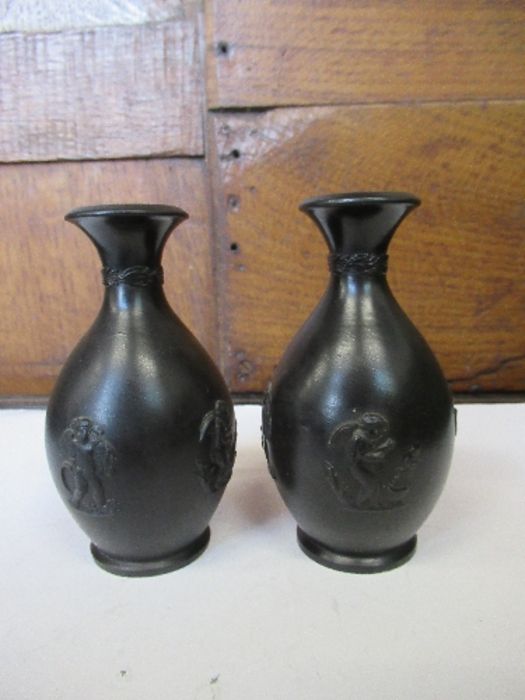A pair of Georgian Wedgwood black basalt bud vases, each with three classical cherub motifs and