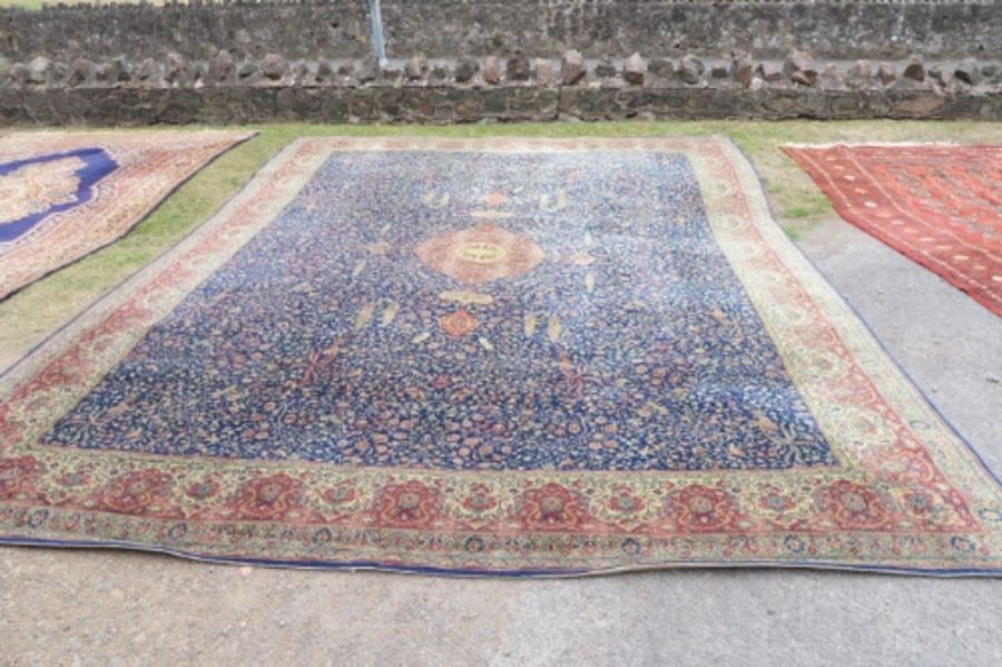 A large Eastern design rug, having a blue ground to a red border, decorated with foliage and