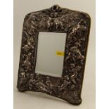 A silver mounted dressing table mirror, decorated with cherubs, with velvet covered back and easel