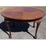 A mahogany quarter veneered oval table, with carved decoration to the scroll leg, terminating in