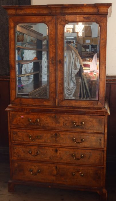 An antique walnut cabinet on chest, the upper section fitted with a pair of mirrored doors,