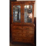 An antique walnut cabinet on chest, the upper section fitted with a pair of mirrored doors,