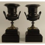 A pair of 19th century mantel urns, in black and gold, on stepped square bases, height 12.5ins