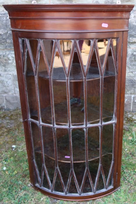 A mahogany barrel front corner cupboard, with fancy glazed door, opening to reveal three shelves,