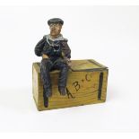 An Early 20th Century Figural Match Striker of a lead sailor sitting on a tin 'Fire' Trunk