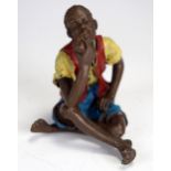 A painted bronze figure of a black man sitting on the ground smoking a pipe, 6cm high.