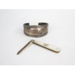 A silver and mother of pearl fruit knife and a white metal cuff, (2).