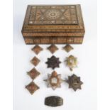 The Devonshire Regiment Cap Badges and lapel badges in a Moorish parquetry box