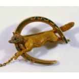 A late 19th century yellow metal hunting brooch in the form of a fox jumping through a horse shoe,