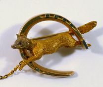 A late 19th century yellow metal hunting brooch in the form of a fox jumping through a horse shoe,