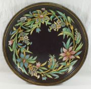A 19th century black toleware circular dish/tray, decorated in enamels with a wreath of flowers,