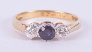 An 18ct yellow gold three stone ring set with a central round cut sapphire and a round brilliant cut