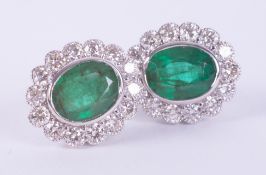 A pair of 18ct white gold cluster style earrings set centrally with an oval cut emerald, total