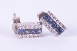 A pair of 18ct white gold earrings set with princess cut sapphires and round brilliant cut diamonds,