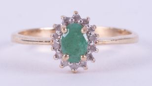 A 9ct yellow gold cluster ring set with a central oval cut emerald surrounded by small