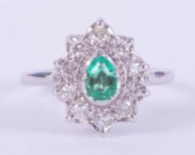 An 18ct white gold cluster style ring set with a central pear cut emerald, approx. 0.32 carats,