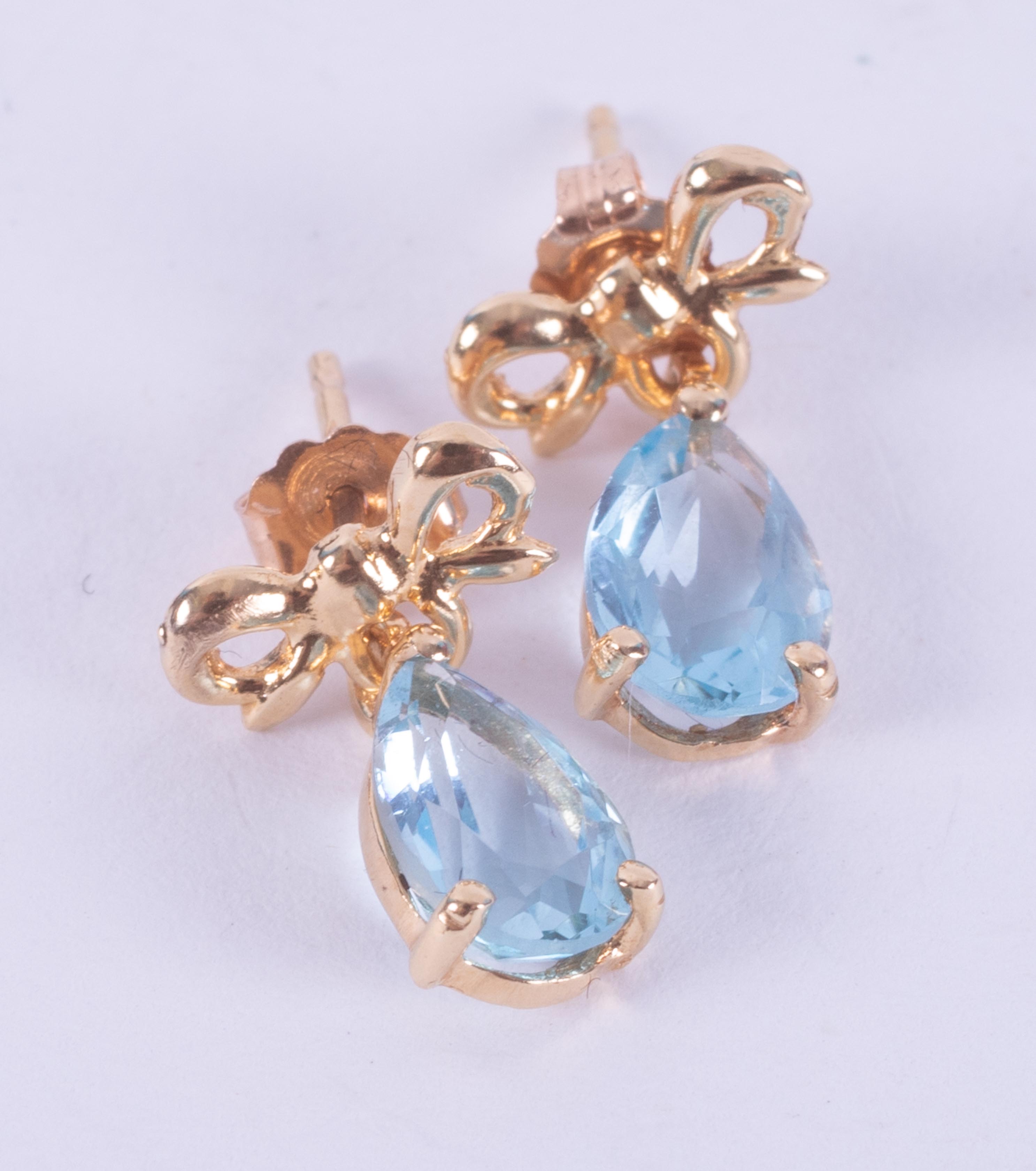 A pair of 18ct yellow gold drop earrings set with a pear shaped blue topaz and a gold bow design