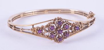 An ornate style 9ct yellow gold bangle set with round cut amethysts in a flower design, hinged, with
