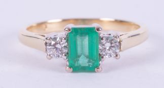 An 18ct yellow & white gold three stone ring set with a central emerald cut emerald, approx. 0.65