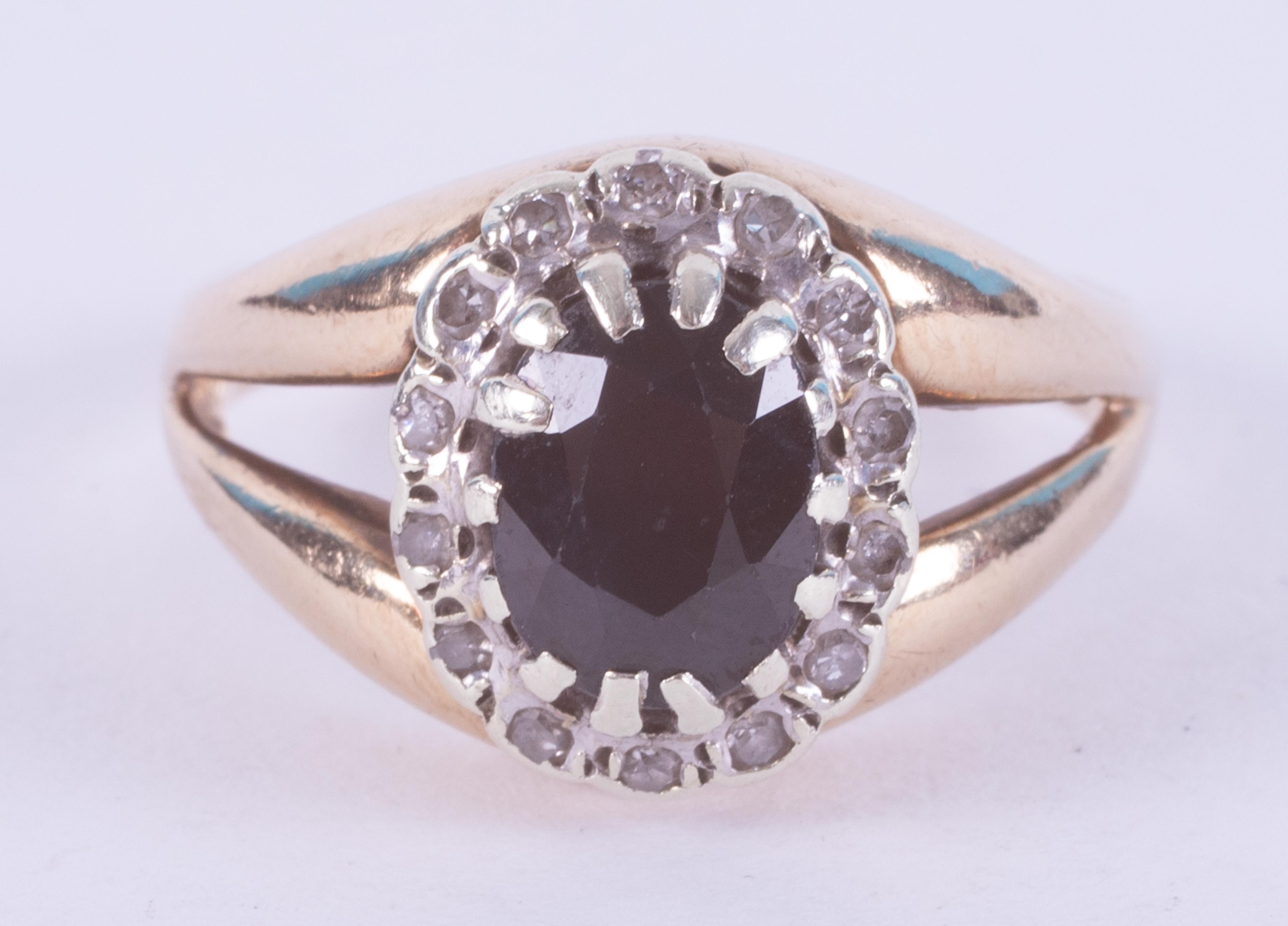 A 9ct yellow gold cluster ring set with a central oval dark blue sapphire and surrounded by tiny