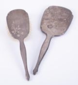 A matching silver backed dressing table mirror and brush, decorated with a flower.