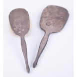 A matching silver backed dressing table mirror and brush, decorated with a flower.