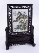 A Chinese table screen with carved wood frame set with a porcelain plaque with landscape scene,