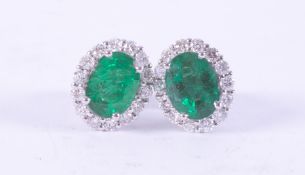 A pair of 18ct white gold oval cluster earrings set centrally with an oval cut emerald, total weight