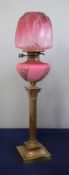 A Victorian oil lamp with a pink reservoir and a pink shade on a brass column base, height 74cm.