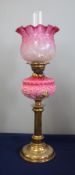 A Victorian oil lamp with pink glass column decorated with flowers and a pink shade on brass base,