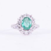 A white gold (indistinctly marked), cluster design ring set with a central oval cut emerald, approx.