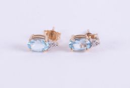 A pair of 9ct yellow gold stud earrings set with an oval cut blue topaz and with a small round cut