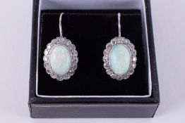 A pair of white gold cluster style drop earrings set with an oval cabochon cut opal, measuring