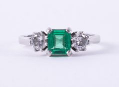 A platinum three stone ring set with a central square cut emerald, approx. 0.80 carats with a